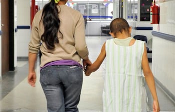 Una niña paciente, camina con su madre por el pasillo de un hospital.