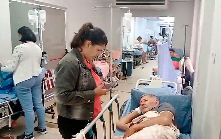 Pasillo de área de Urgencia del Hospital Central, lleno de pacientes que esperan en sillas o camillas por una cama de internación. 