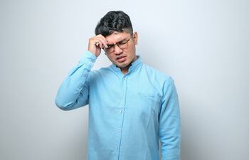 Un joven con anteojos se toca la sien en señal de dolor de cabeza.