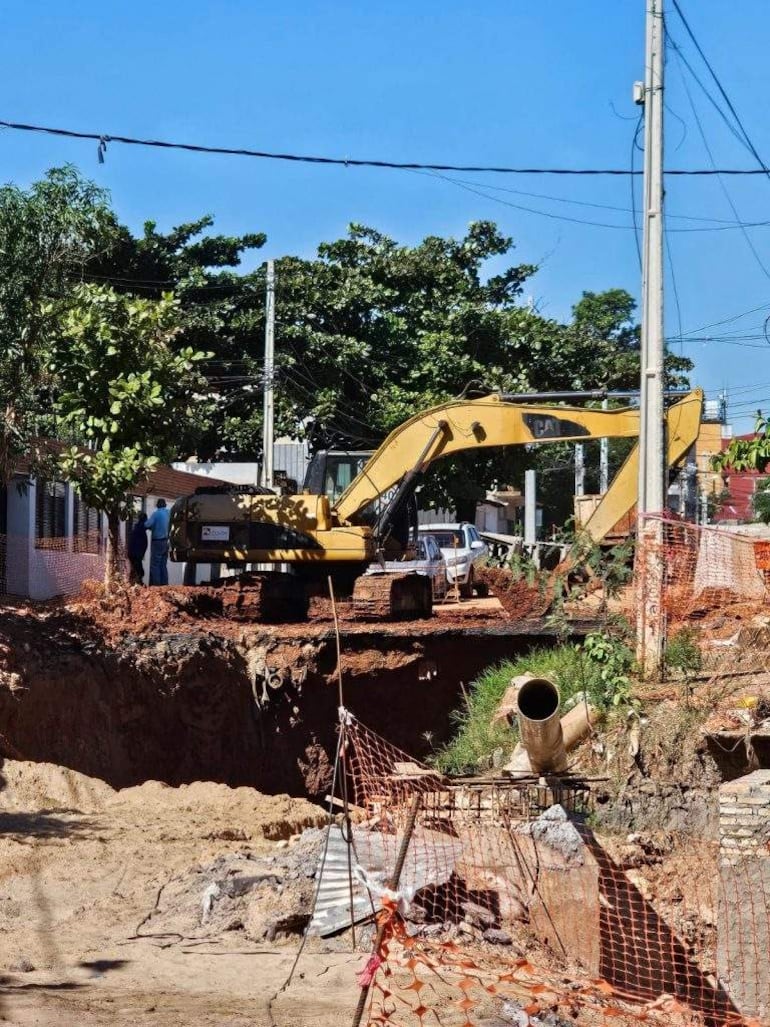 Excavadora amarilla Caterpillar trabaja en un terraplén mientras un hombre observa de lejos, rodeado por cercas de seguridad.