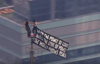 Dos personas en prendas oscuras sostienen un gran banner negro con letras blancas en la cima del Empire State Building.