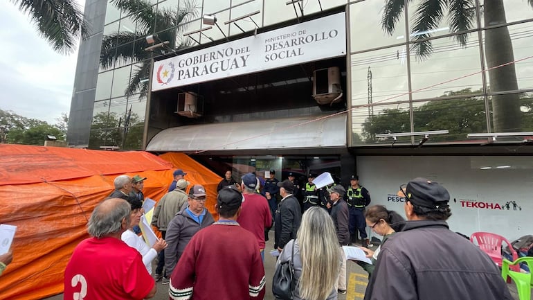 Grupo de personas mayores con documentos, algunas de ellas usando sombreros, frente al Ministerio de Desarrollo Social.