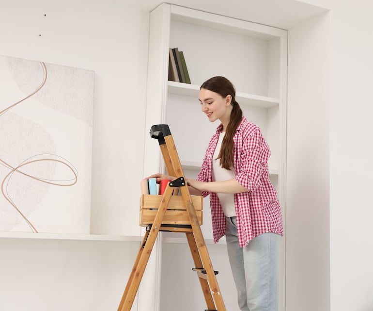 Concepto de puttering. Mujer reordena libros en un estante de casa.