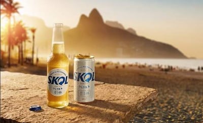 Botella y lata de Skol en mesa de piedra, rodeadas de palmeras y montañas durante el atardecer.