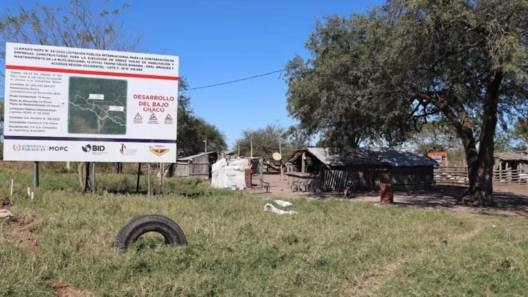 Cartel informativo sobre licitación de obras viales en área rural, con estructuras de madera y terreno cubierto de hierba.