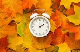 Reloj despertador contra un fondo de hojas otoñales.