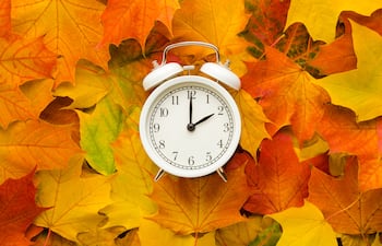 Reloj despertador contra un fondo de hojas otoñales.