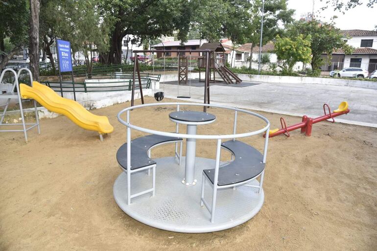 Estructuras de juegos en el parque infantil, rodeadas de árboles y césped, sin personas presentes.