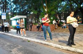 Pasajeros apostados en una parada sobre la avenida Mariscal López, frente a la plaza Infante Rivarola del barrio Villa Morra, observan sus celulares para sobrellevar la larga espera.