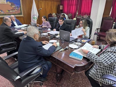 Isaías Ricardo Fretes habla en mesa rodeada por Hassel Jimmy Jiménez y Bettina Albertini, todos revisando documentos en sala con decoración roja.