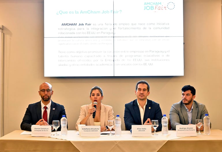 Cuatro personas en un panel: hombre calvo con barba y corbata roja, mujer con blazer claro, hombre con traje y joven con traje claro, en evento formal.