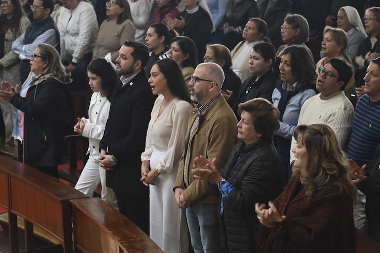 Cuatro personas al frente, una mujer con blusa blanca y otra con chaqueta negra, en un ambiente solemnemente festivo.