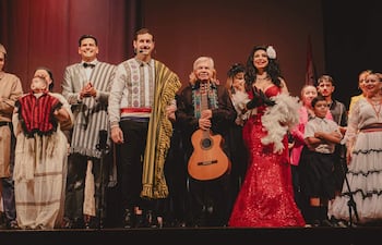 Margarita Franco en vestido rojo brillante sostiene plumas, rodeada de músicos y espectadores aplaudiendo con alegría.
