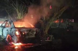 Automóvil en llamas en el entorno nocturno, rodeado de árboles y humo visible en una zona al aire libre.