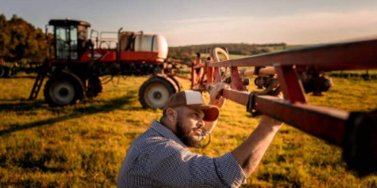 Un hombre manipula maquinaria agrícola en un campo abierto, reflejando la labor rural.
