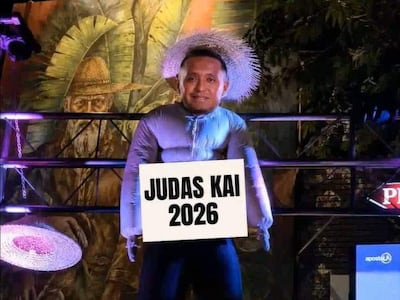Muñeco con cabeza humana, vestido de azul y sombrero de paja, sostiene cartel 'JUDAS KAI 2026' en un ambiente festivo. Imagen extraída de las redes sociales.