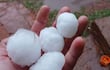 Mano sostiene piedras de granizo en un terreno mojado y césped verde, evidenciando el fenómeno climático reciente.