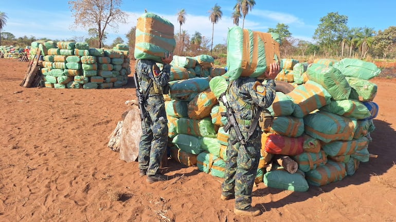 Dos miembros de fuerzas de seguridad en uniforme camuflado sostienen paquetes de marihuana en un ambiente árido.