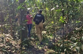 Grupo de personas camina por un área boscosa, uno porta chaqueta con la palabra 'POLICÍA', rodeados de vegetación verde.