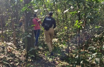 Grupo de personas camina por un área boscosa, uno porta chaqueta con la palabra 'POLICÍA', rodeados de vegetación verde.