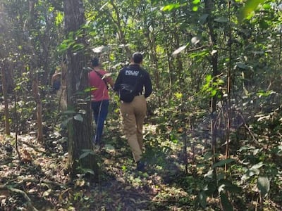 Grupo de personas camina por un área boscosa, uno porta chaqueta con la palabra 'POLICÍA', rodeados de vegetación verde.