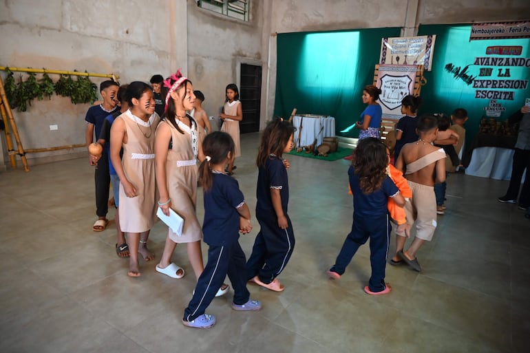 Grupo de niños de la escuela Yva Viju Miri interactuando en un evento cultural, con vestimenta variada y un adulto facilitador al fondo.