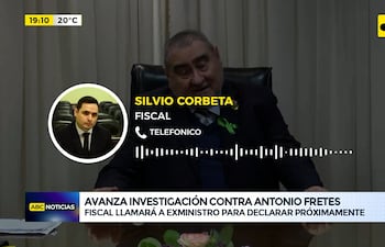 Silvio Corbeta, en traje oscuro, habla con un hombre de camisa azul en un entorno de oficina con cortinas y escritorio.