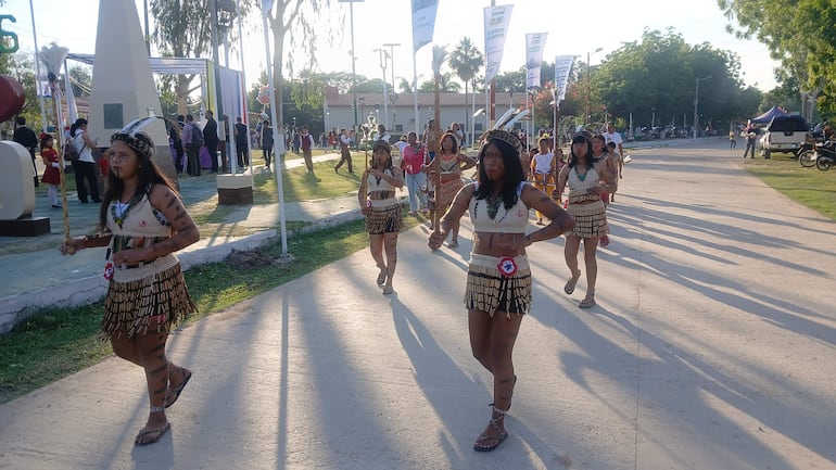 Siete mujeres vestidas con trajes tradicionales y faldas de flecos desfilan en Fuerte Olimpo, rodeadas de un ambiente festivo.