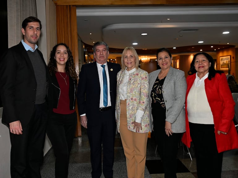 Seis personas posan en un salón elegante, con tres hombres y tres mujeres vistiendo abrigos y chaquetas, todos sonriendo.