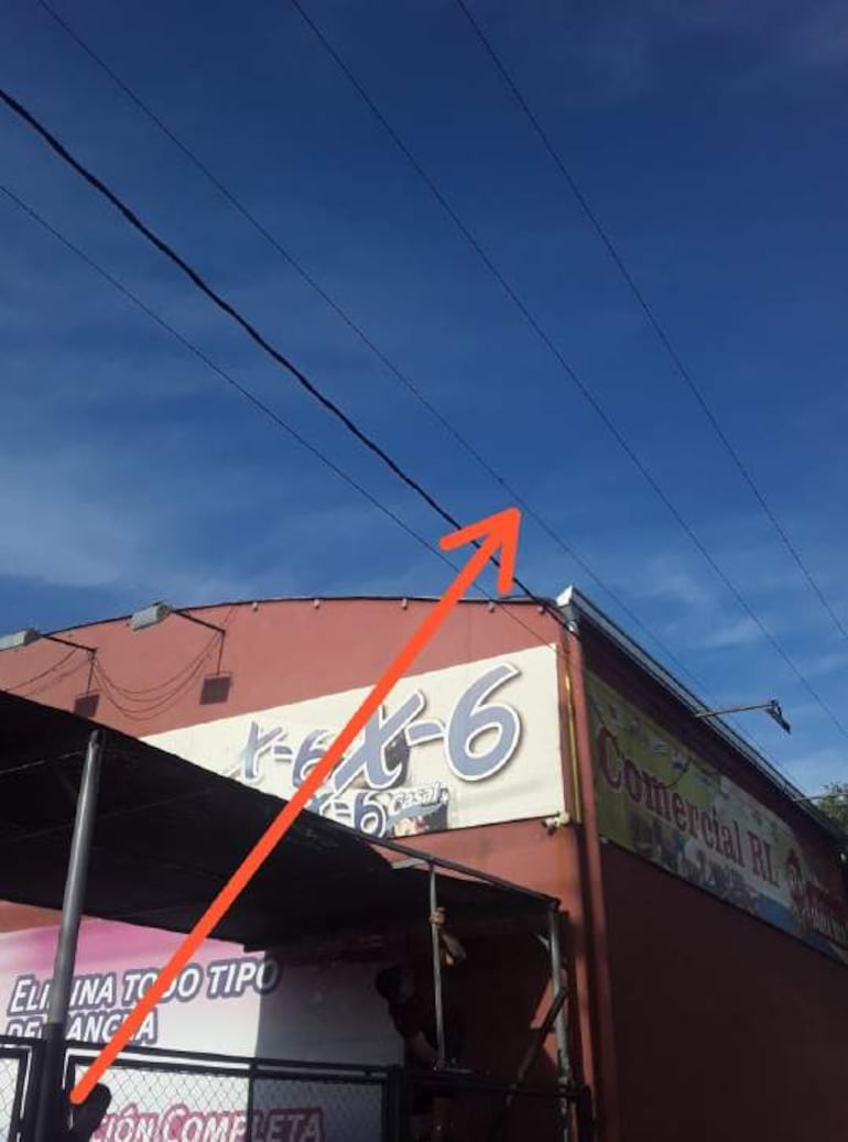 Fachada de un edificio rojo con cartel comercial y cables eléctricos visibles en un cielo despejado.