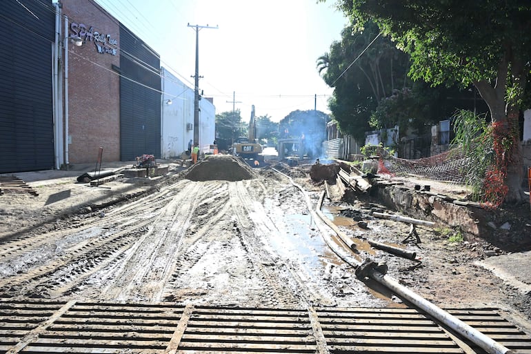 Escena de obra en construcción con maquinaria pesada, montones de tierra y malla de seguridad delimitando el área.