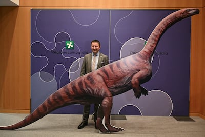 Franco Claretti, director del área de Lombardía del Parque Nacional del Stelvio, posa para una fotografía con un dinosaurio de cartón durante una conferencia de prensa para presentar el descubrimiento de miles de huellas de dinosaurios halladas en el Parque Nacional del Stelvio, en Italia, cerca de las zonas que albergarán los Juegos Olímpicos de Milán-Cortina 2026, en Milán, el 16 de diciembre de 2025.
