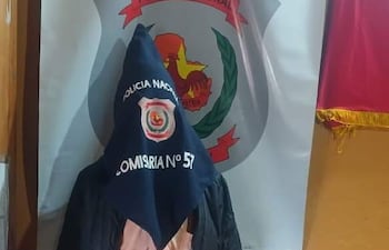 Hombre cubierto con trapo de la Policía Nacional, en comisaría con escudo visible, vestido con saco negro y camisa clara.