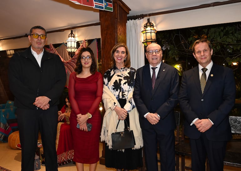 César Diesel en traje oscuro y gafas, junto a mujeres sonrientes, en un ambiente acogedor y decorado.