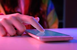 Mano femenina interactuando con un smartphone sobre una superficie clara, con iluminación púrpura y roja en un ambiente interior.