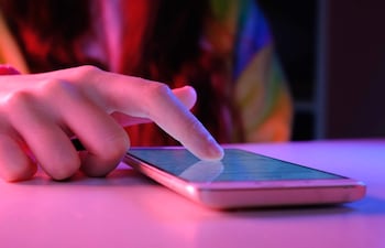 Mano femenina interactuando con un smartphone sobre una superficie clara, con iluminación púrpura y roja en un ambiente interior.