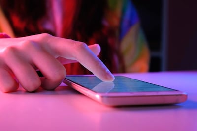 Mano femenina interactuando con un smartphone sobre una superficie clara, con iluminación púrpura y roja en un ambiente interior.