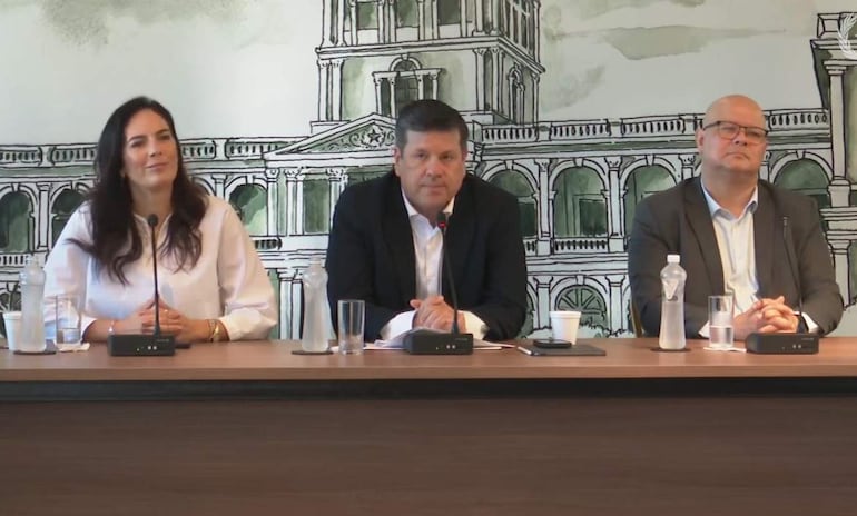 Javier Giménez en camisa blanca y saco negro, Claudia Centurión en blusa blanca y Óscar Lovera en saco marrón y camisa blanca, en conferencia con ambiente moderno.
