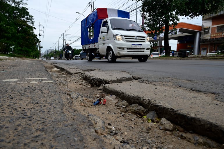 Camioneta de carga blanca con toldo en colores de la bandera paraguaya circula por Avenida Artigas con pavimento deteriorado.