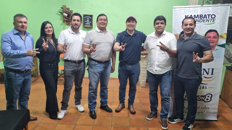 Carlos Achón y Felisa Roldán sonríen, mientras otros posan en grupo con gestos de paz en fondo verde.