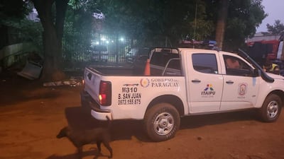 Camioneta blanca del Gobierno del Paraguay y policía, con un perro negro en el entorno iluminado y nocturno.