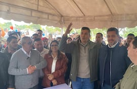 Santiago Peña, con gafas, habla levantando la mano, mientras Pedro Alliana escucha atento bajo una carpa con otros individuos.