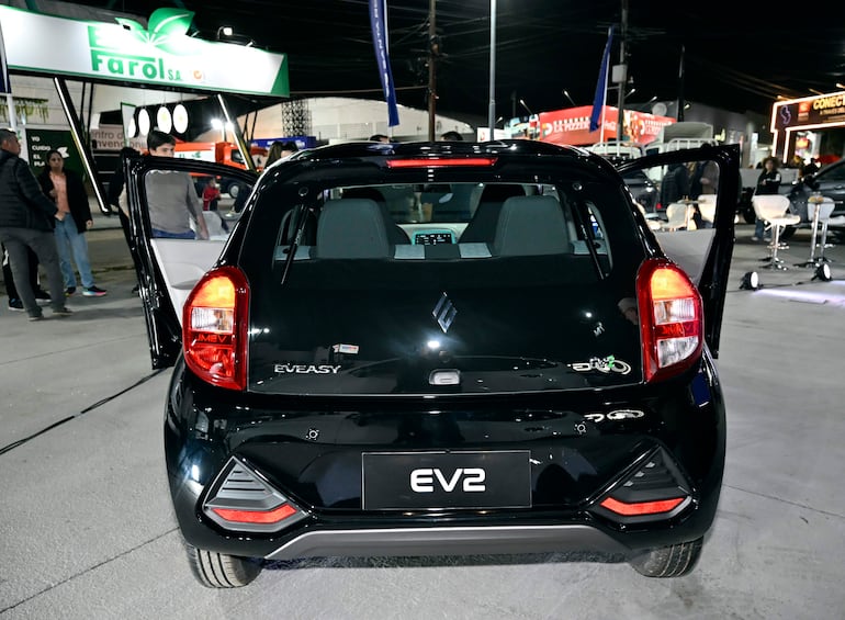 Automóvil negro Suzuki EV2 con puerta trasera abierta, asientos grises, rodeado de un grupo de personas en un evento nocturno.