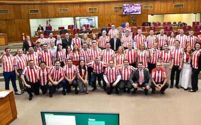 Diputados sonrientes, vistiendo camisetas de rayas rojas y blancas, organizados en filas en un ambiente institucional.