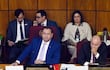 Ramon Retamozo en traje azul con corbata clara, rodeado de senadores en un ambiente legislativo de fondo de madera.