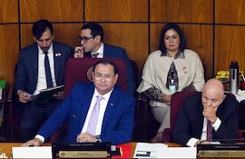 Ramon Retamozo en traje azul con corbata clara, rodeado de senadores en un ambiente legislativo de fondo de madera.