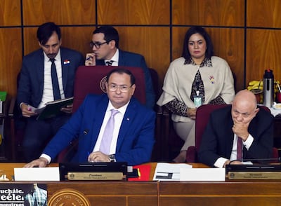 Ramon Retamozo en traje azul con corbata clara, rodeado de senadores en un ambiente legislativo de fondo de madera.
