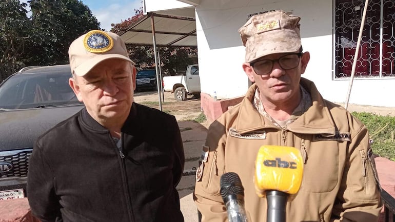 César Silguero con gorra clara y chaqueta negra, Ángel Franco con gorra camuflada y abrigo claro, hablando en micrófono en evento formal.