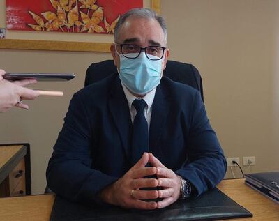 Humberto Otazú sentado en un escritorio con traje oscuro y mascarilla, manos juntas, en un ambiente de oficina profesional.