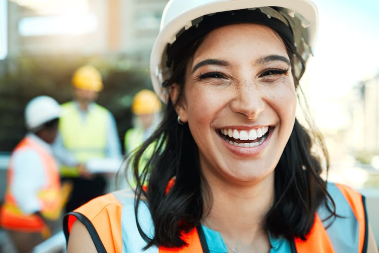 Mujer sonriente con un casco y chaleco en una obra en construcción